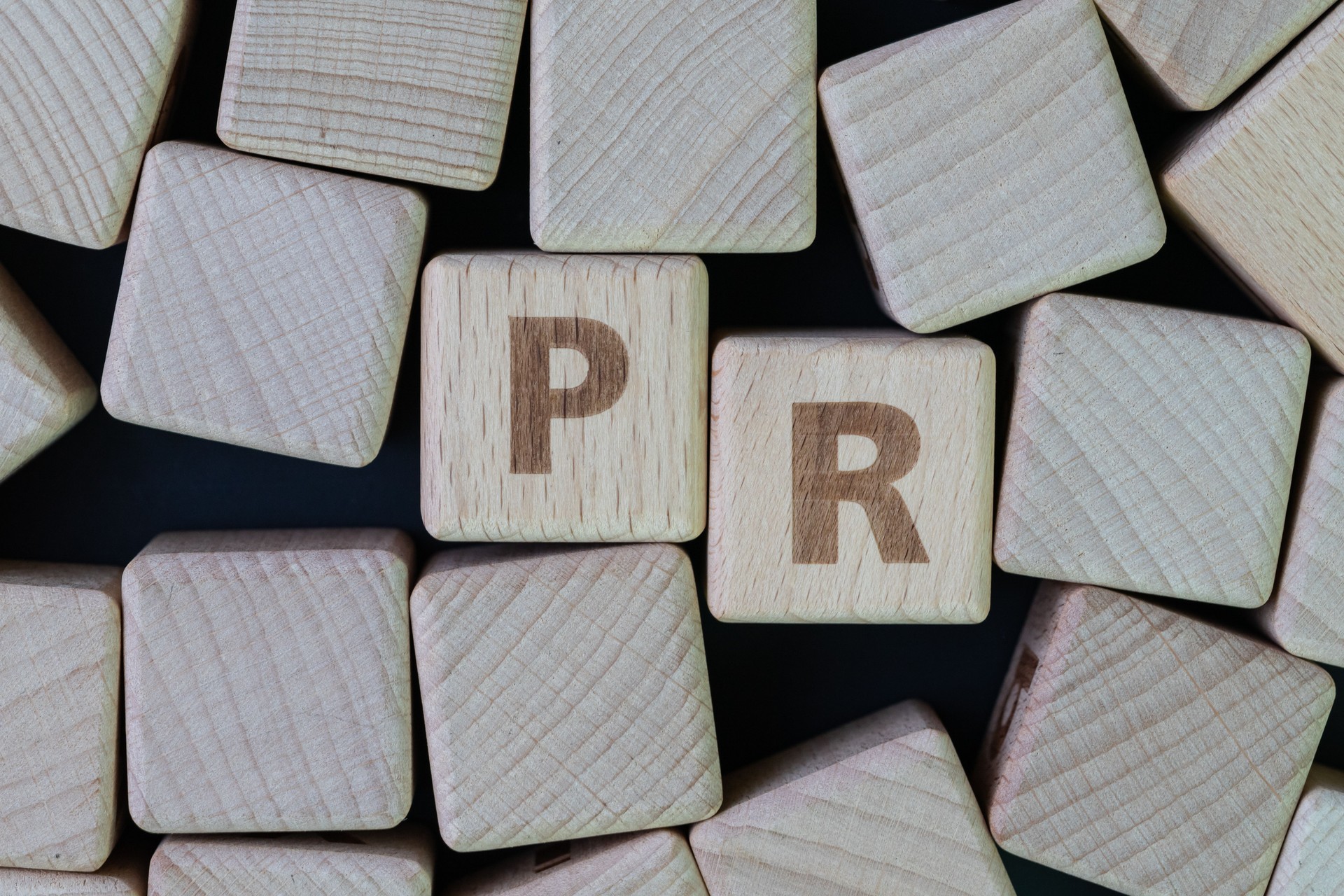 PR, public relation company or corporate communication concept, cube wooden block with alphabet combine the word PR on black chalkboard background